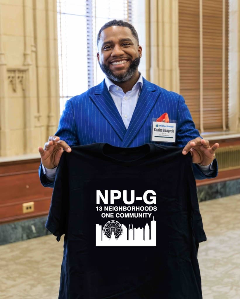 Charles Bourgeois holding an NPU-G 13 Neighborhoods One Community skyline tee